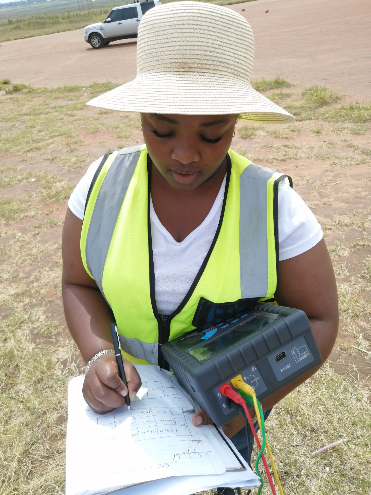 Field worker writing in a notebook while holding a connected earth tester