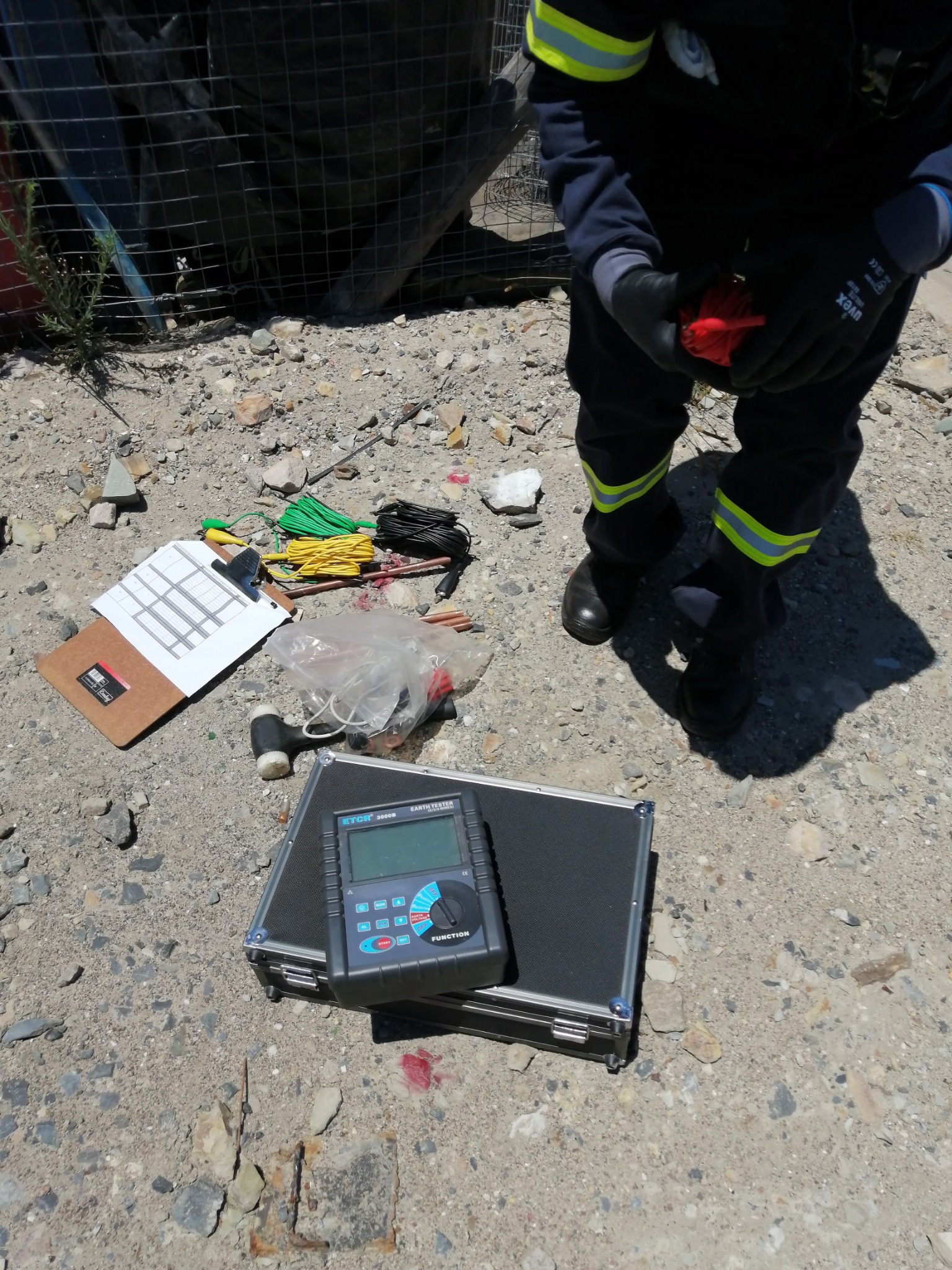 Tester, carrying case, clipboard, leads and stakes arranged on rocky ground